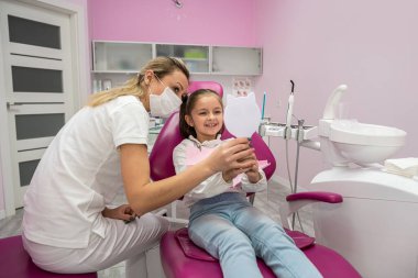 little female patient in the dental chair looks at her teeth after their treatment. dental office. mirror in hands