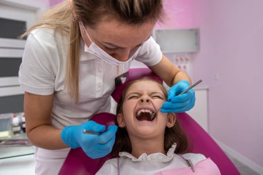 Tatlı küçük kız dişçi koltuğuna oturur ve ağrıyan dişleri tedavi eder, surat yapar. Ağız boşluğunun tedavisi. dişçilik