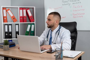  Doktor bey masamızda oturup dizüstü bilgisayarını kullanarak tıbbi temalar ve işyeri eğitimi alıyor. Sağlık personeli