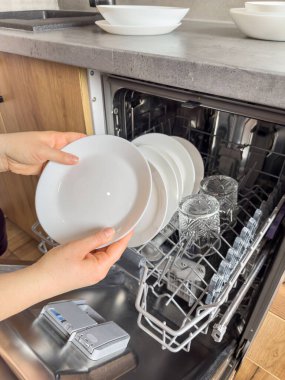 Bulaşık makinesinden temiz bulaşıkları çıkaran kadını kapatın. Ev hanımı ev işlerini yapar.