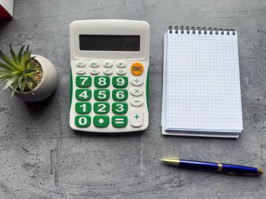 Hesap makinesi, defter ya da not defteri ve gri masadaki tükenmez kalem. Kopyalama alanı olan üst görünüm