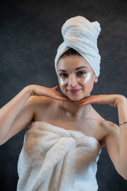 Beyaz havlulu neşeli genç kadın siyah üzerine izole edilmiş göz altındaki pürüzsüz cilt için kolajen bandı uyguladı. Yaşlanma önleme prosedürleri