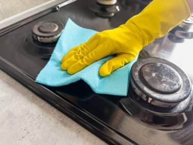 Sarı eldivenli ünlü bir el mutfak sobasını kuru süngerle siler. Ev temizleme servisi