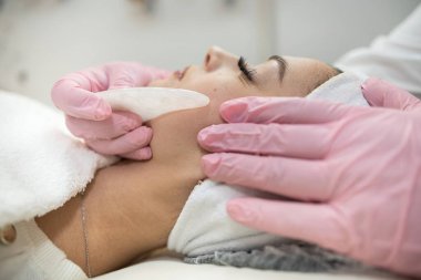 Kozmetik uzmanı müşterinin yüzüne beyaz guaj kazıyıcı sürerek tıbbi işlem yapıyor. Sağlık yaşam tarzı