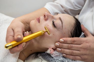 beautician makes procedure use vibrating electric facial massager for her female client, face skin youthfull and wellness clipart