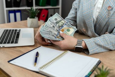 İş kadını bir dolar sayıyor, boş not defteri, iş yerindeki kalem bilgisayarı. Finans kavramı