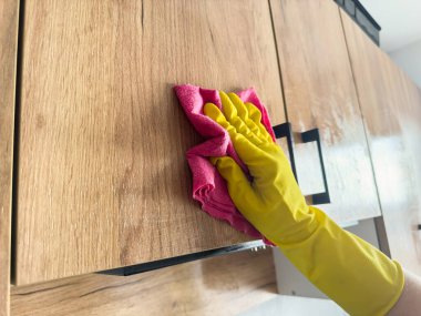 Sarı lastik eldivenli kadın eli, ahşap mutfağı temizleyen bir bez kullanıyor. Ev işi kavramı