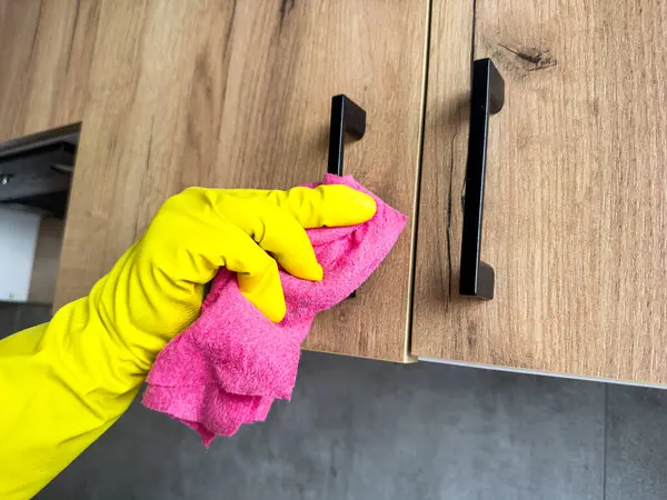 Yakın plan kadın elleri sarı lastik eldivenler ve bez temizleme servisi modern stil mutfakta ahşap tezgahı siliyor.