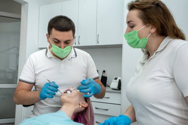 Erkek dişçi, dişçi muayenehanesinden memnun bir bayan müşteriye asistanıyla tedavi uyguluyor. İnsanlar konuşur ve birbirlerine bakarlar. - İnsanlar. ilaç