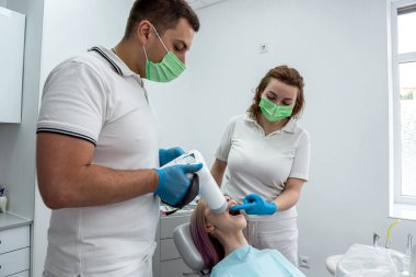 male dentist is photographing the teeth of a girl patient next to a female assistant. The concept of a dental clinic