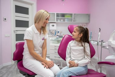children's dentist conducts a consultation for a little girl in a dental chair. children's dentistry. the doctor talks about the importance of oral care