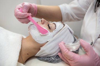 Güzellik uzmanı kadın müşterinin yüzüne beyaz maske takıyor, güzellik merkezinde tedavi görüyor. Sağlık cilt bakımı kavramı