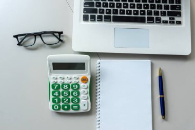 Not defterini kalem dizüstü bilgisayarı ve hesap makinesi olan beyaz ofis masasında notlar için aç. Üst görünüm.