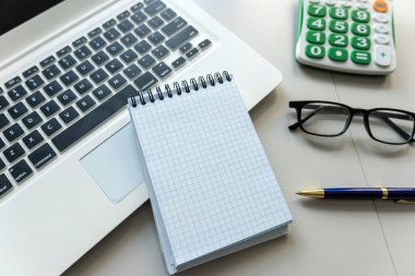 Not defterini kalem dizüstü bilgisayarı ve hesap makinesi olan beyaz ofis masasında notlar için aç. Üst görünüm.