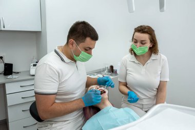 İki dişçi, bir erkek ve bir kadın ağzını açık tutan güzel bir kadın hastanın hasta dişlerini tedavi eder. Oral sağlık. dişler