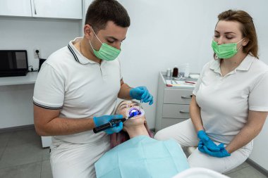 Erkek ve dişi dişçiler hastanın dolgularını sertleştirmek için ultraviyole lamba kullanırlar. dişçi dişleri