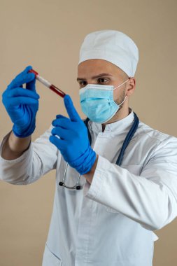 Üniformalı maske takan erkek doktor ve eldivenler test tüpündeki kana bakıyor. Sağlık hizmeti, bilim konsepti. 
