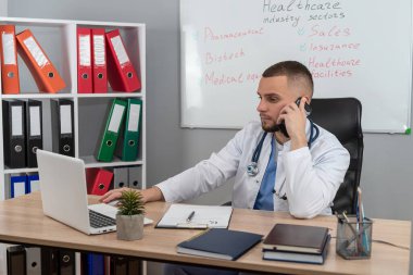  Doktor bey masamızda oturup dizüstü bilgisayarını kullanarak tıbbi temalar ve işyeri eğitimi alıyor. Sağlık personeli