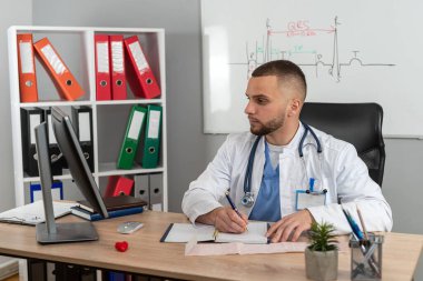 Beyaz üniformalı, steteskop işi olan beyaz bir doktor, çalışma masasında oturuyor.