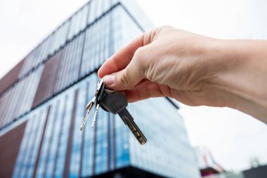 Erkek emlakçı yeni modern cam binaya karşı yeni ev dairesinin anahtarlarını gösteriyor.