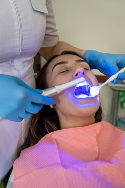  Kadın hastaya UV lambası ile diş beyazlatma prosedürü uygulanıyor. Sağlık Hizmetleri