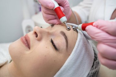 Genç ve güzel bir kadın spa kliniğindeki terapistten canlandırıcı bir yüz bakımı alıyor. Yüz gerdirme prosedürü