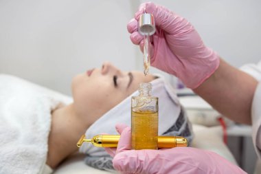 Güzellik uzmanlarının ellerine yakın çekim, kaplıca salonundaki genç kadınların yüzüne pipetle birkaç damla yağ damlatıyor. Yüz dermatolojisi prosedürü, cilt bakımı