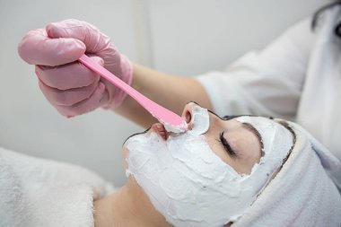 Genç bayan müşteri güzellik salonundaki beyaz maskeden yüz bakımı alıyor. Cilt bakımı kavramı