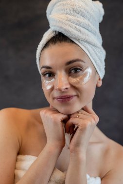 Göz bandı takmış mutlu bir kız siyahın üzerinde yaşlanma karşıtı prosedürler uyguluyor. Cilt bakımı