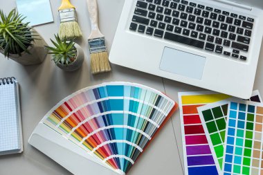 Ofis masası, renkli kumaş örnekleri bilgisayar dizüstü bilgisayarı, boş not defteri kalemi. Yaratıcı grafik kavramı