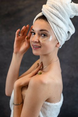 Siyah arka planda izole edilmiş siyah silikon bantları olan beyaz havluyla temiz ciltli genç tatlı bir kız. Cilt bakımı için yamalar göz altı koyu halkalar