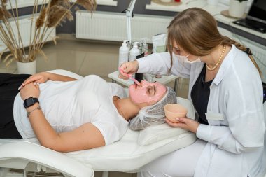 Güzel beyaz bir kadın güzellik salonunda pembe kilden bir maske takıyor. Spa tedavisi kavramı