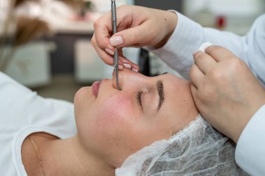 Güzellik uzmanı, güzellik salonundaki genç bayan müşteri tarafından manuel yüz temizleme yapıyor. Yaşlanma önleme prosedürleri