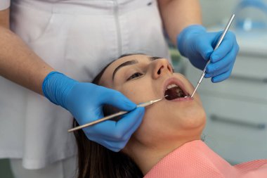 Diş çürüklerine ya da diş eti hastalıklarına tıbbi aletlerle bakan bir dişçi. Diş hekiminden tedavi