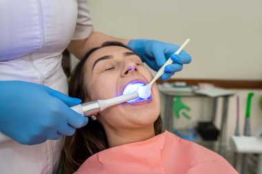 Diş hekimi, dişlerini beyazlatmak için mor ötesi lamba ve fotopolimer karışımı kullanıyor. Diş sağlığı ve sağlık hizmetleri kavramı