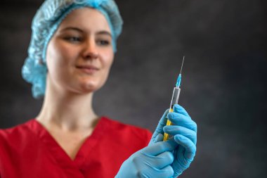 Kırmızı paltolu kadın doktor, karanlıkta izole edilmiş koronavirüse karşı enjeksiyon için bir şırınga tutuyor. Aşılama kavramı