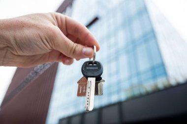 Adam evin anahtarlarını cam binaya karşı tutuyor. Yatırım yeni apartman konsepti