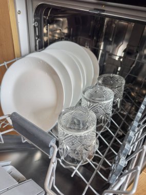 Tabaklarında temiz tabaklar ve bardaklar olan bulaşık makinesini aç. Ev temizleme süreci