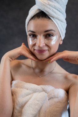 Beyaz havlu takan bir kız şişkinlik için göz bandı kullanıyor. Siyaha izole edilmiş kırışıklıklar. Cilt bakımı için siyah kolajen bantları 