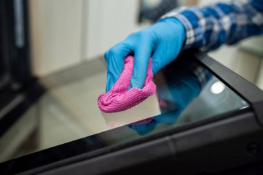 Koruyucu eldivenli bir işçinin kadın elleri fırını bir bez ve spreyle temizleyip temizliyor. Kadınların elleri temizlendi. Eller yukarı.