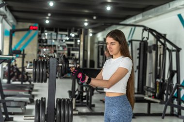  Spor salonunda halter için ağır bir plaka taşıyan genç atletik kadın egzersizi. Kuvvet ve motivasyon