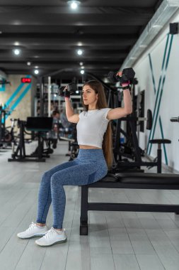 Beyaz tenli kadın antrenör ağırlık kaldırıyor ve spor salonunda pazılarını çalıştırıyor. Spor da sağlıklı bir yaşam tarzı.