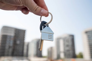 Kendine güveni tam olmayan bir şahıs, inşaat aşamasında olan ve henüz tamamlanmamış büyük bir binanın önünde bir dizi anahtar tutuyor.