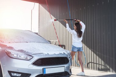 Güzel bir kadın otomobil tabancasını köpükle yıkıyor dışarıda oto yıkama istasyonunda. Servis aracı