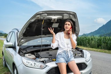 Kadın, yolda bozuk bir arabanın yanında telefon kulübesinde konuşuyor. Motor, sürmeye devam etmeyi imkansız kılıyor.