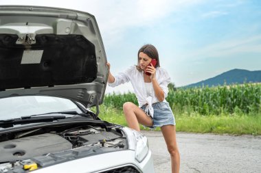  Kadın sürücü dışarıda bozuk arabasının motoruna bakıyor. Yaz gezisinde servis otomatiği