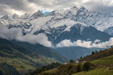 Sahnede, arka planda görkemli bir şekilde yükselen güzel karlı bir sıradağ var. Önplanda huzurlu bir nehir akıyor.