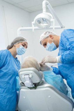 Dişçi-ortopedi doktoru ve asistanı klinikte emekli genç bir kadını muayene ediyorlar.