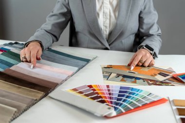 Kadın tasarımcı ev planı taslağını tutuyor ve renkli doku kalıntılarını seçiyor. İç tasarım