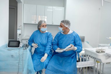 İkinci takım dişçi cerrahının portresi mavi ceketli maske eldivenli klinikteki dişçi odasında. Takım çalışması.